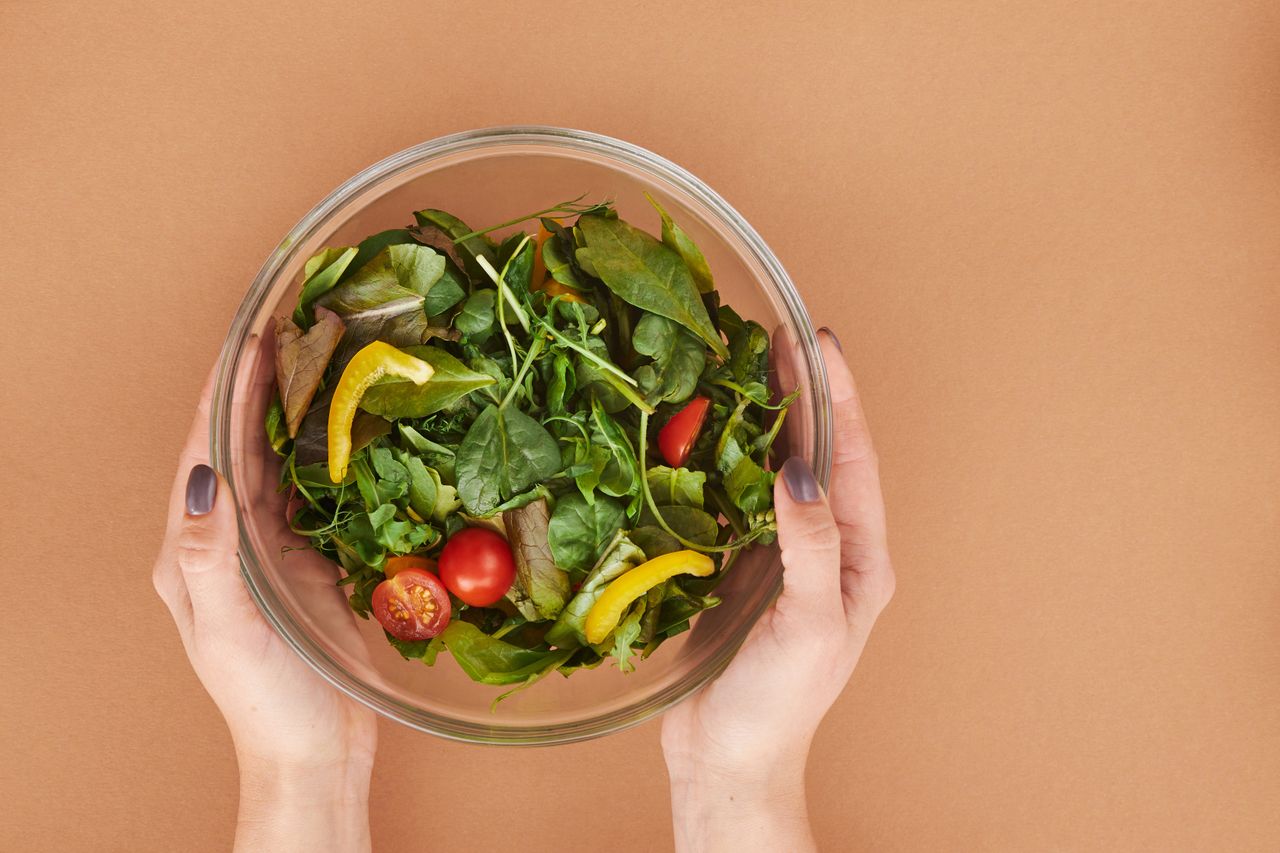 journey Healthy fresh salad bowl with cherry tomatoes and greens held by hands on a brown surface.